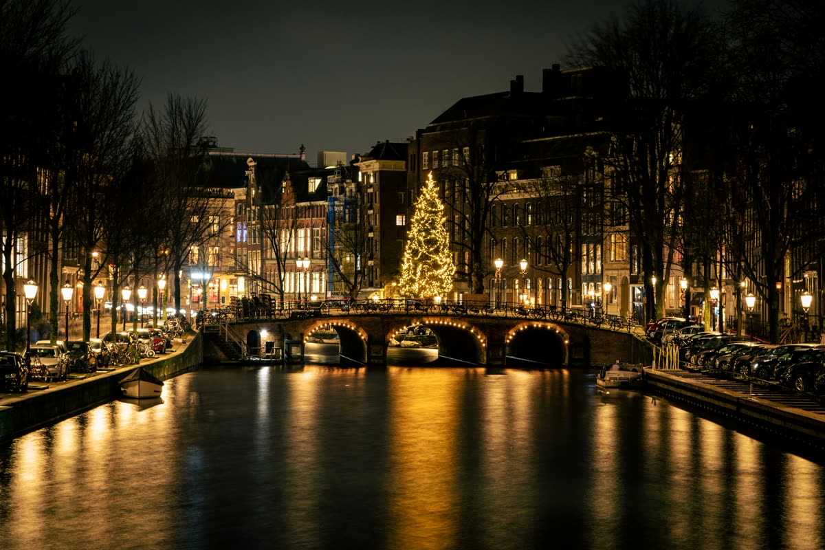 An Amsterdam canal at night in December, with a lit Christmas tree on the bridge
