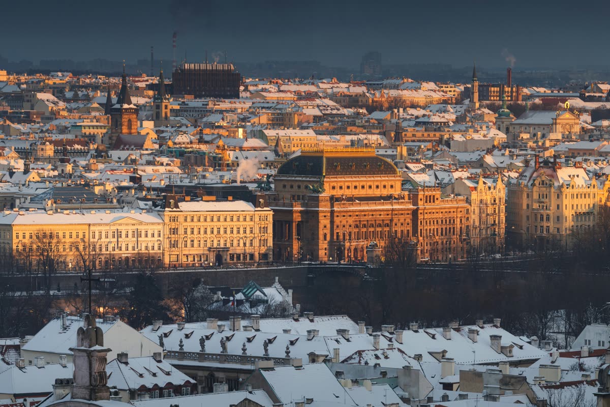 Snow on the rooftops of Prague, with the National Theatre in low winter sun