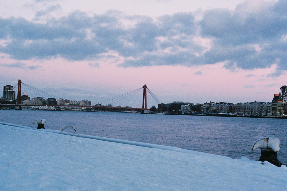 The red Willemsbrug across the Maas at dusk, seen from a snowy quay in Rotterdam